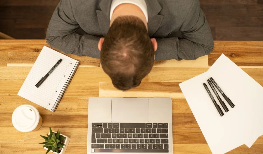 Professional overwhelmed at work with head down near computer